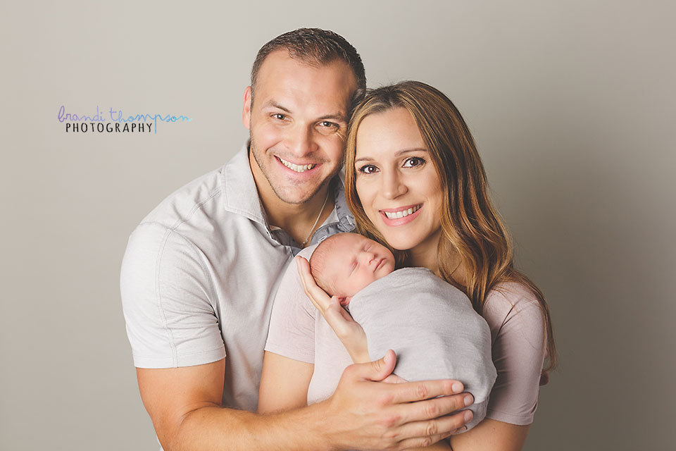 newborn photography - smiling white man and woman holding sleeping baby - newborn parent image