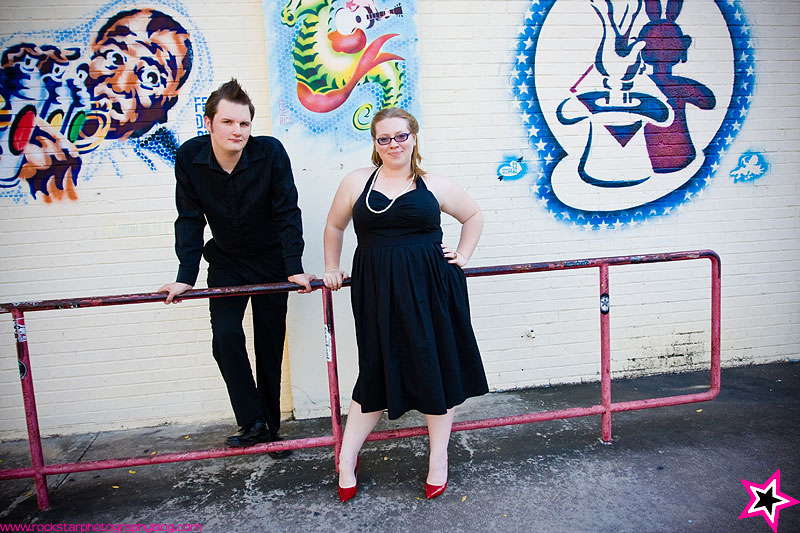 a couple dressed in black in front of a wall with graffiti on it - posing plus size clients