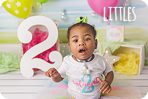 a two year old Black girl with trach in a white shirt with a colorful background and the number two, text says littles