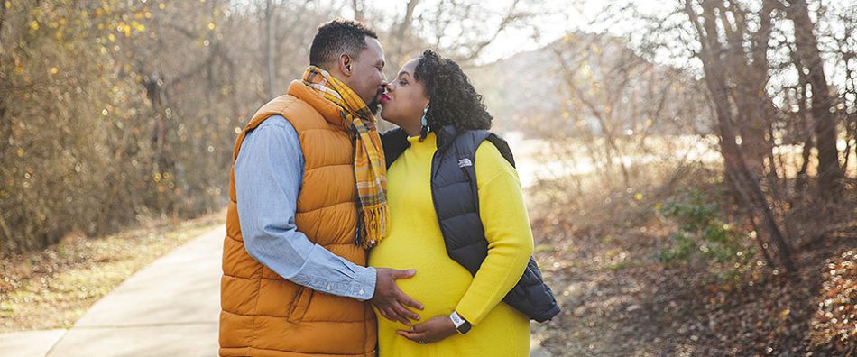 a black couple with a pregnant woman, kissing while wearing bright, winter clothing