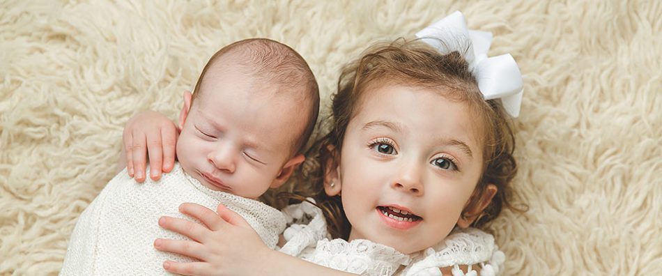 a white newborn boy and toddler girl on a cream colored rug.