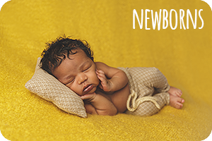 a black basby boy with curly hair, asleep on a dark yellow backdrop with a tan pillow and pants, text says 'newborns'