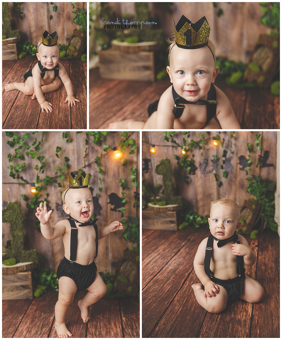 a light skinned one year old boy in a studio set with brown wood look background with greenery and black wild thing silhouettes . He is wearing a black diaper cover, suspenders and a gold crown with a 1 on it
